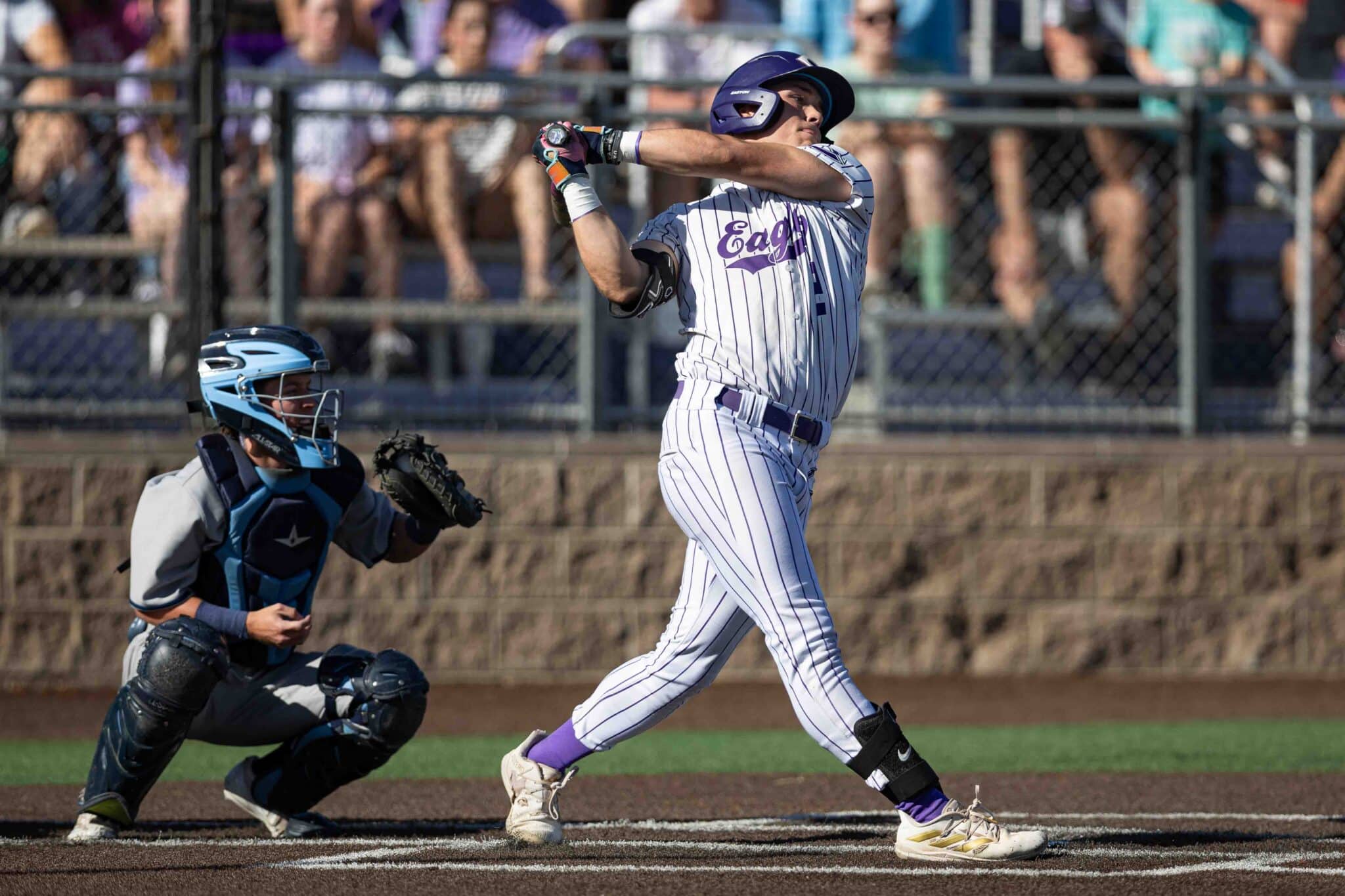 Baseball batter in white pinstripe uniform swinging at a pitch, catcher crouched behind him.
