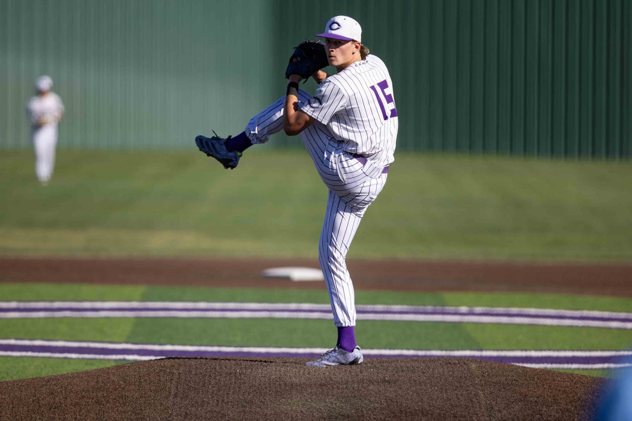 Baseball pitcher in a white pinstripe uniform delivering a pitch on the mound with leg raised and glove near face.