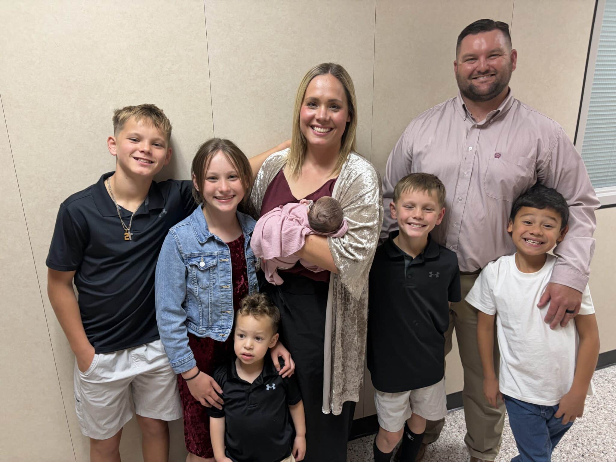 Group of seven people posing for a photo in a hallway, smiling at the camera.