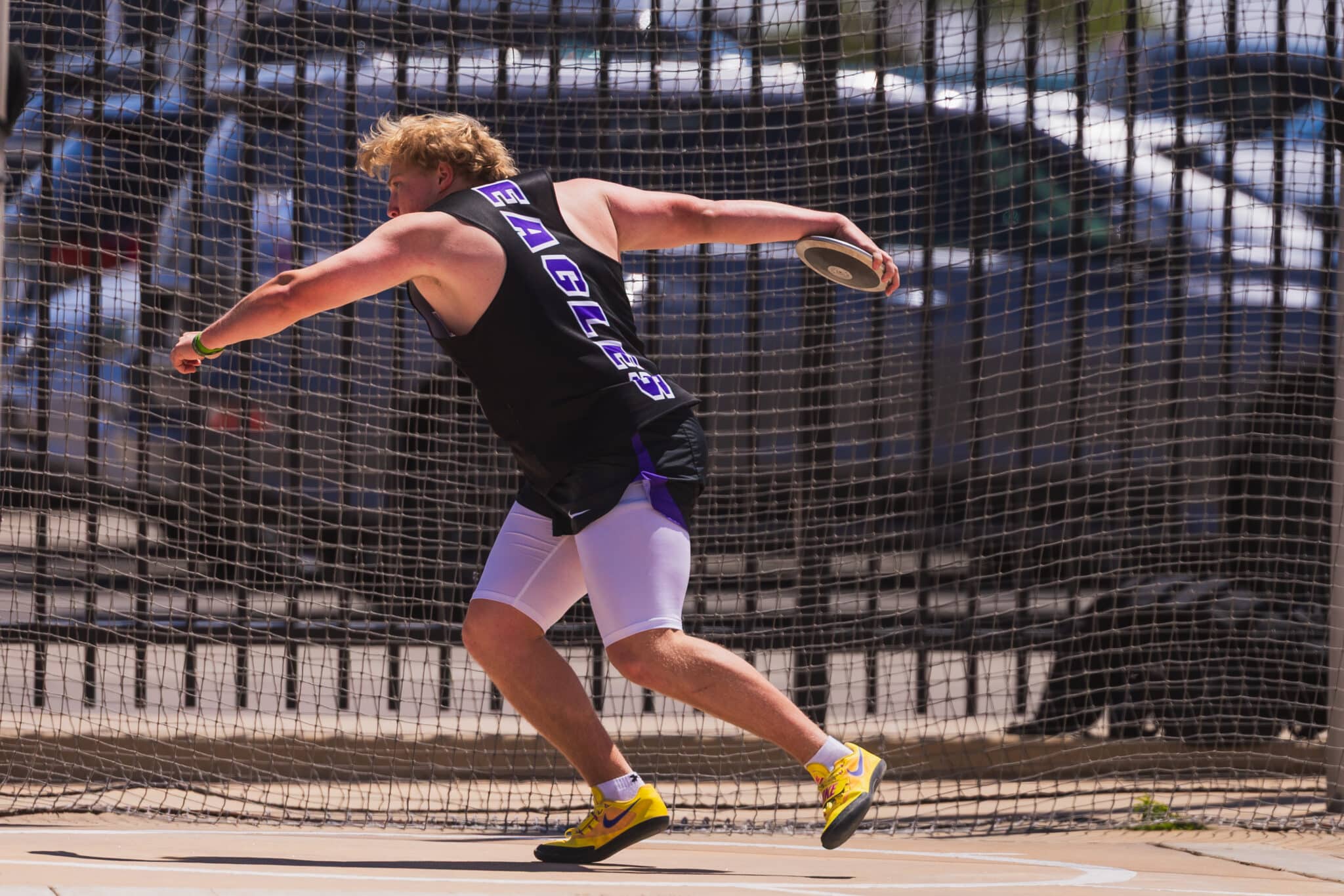 Athlete in a black jersey labeled 'EAGLES' throwing a discus inside a fenced throwing area.