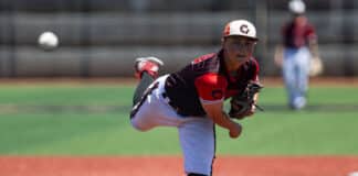 Baseball pitcher in red and black uniform delivering a pitch on the mound, ball in midair nearby.