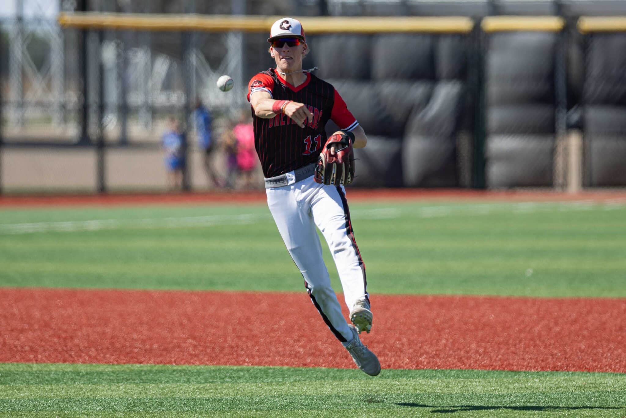 Baseball pitcher in a red-and-black uniform winds up to throw a pitch on a baseball field.