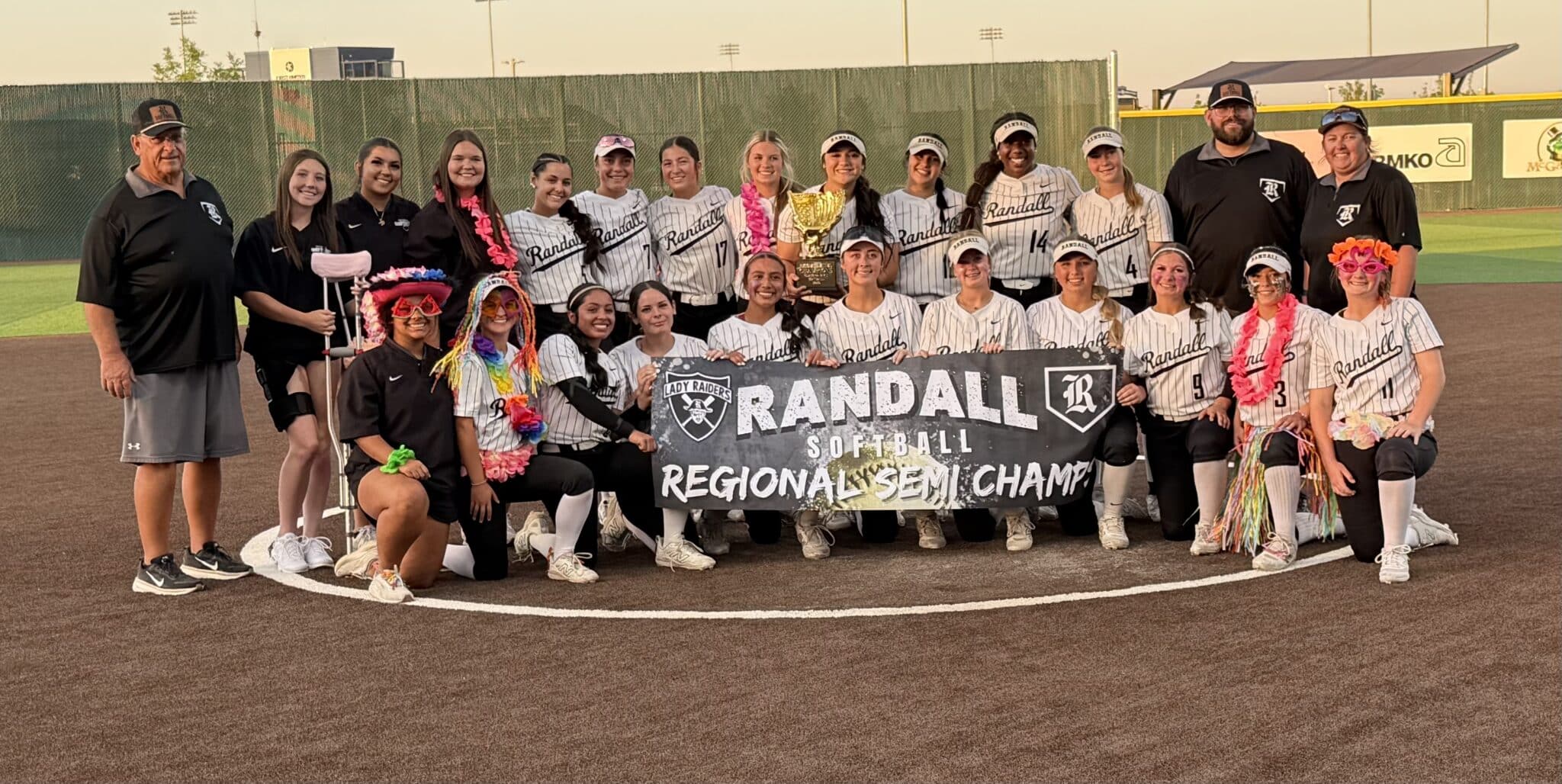 IMG_0310 | Press Pass Sports Girls softball team posing on the field with a trophy and banner that reads Randall Softball Regional Semi Champs.