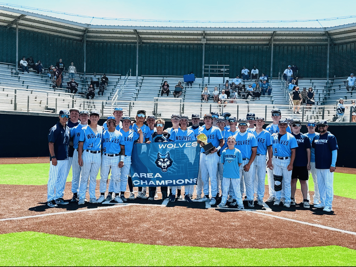 Baseball team in light-blue uniforms posing on the infield with a blue banner reading 'WOLVES AREA CHAMPIONS' and a trophy in front.