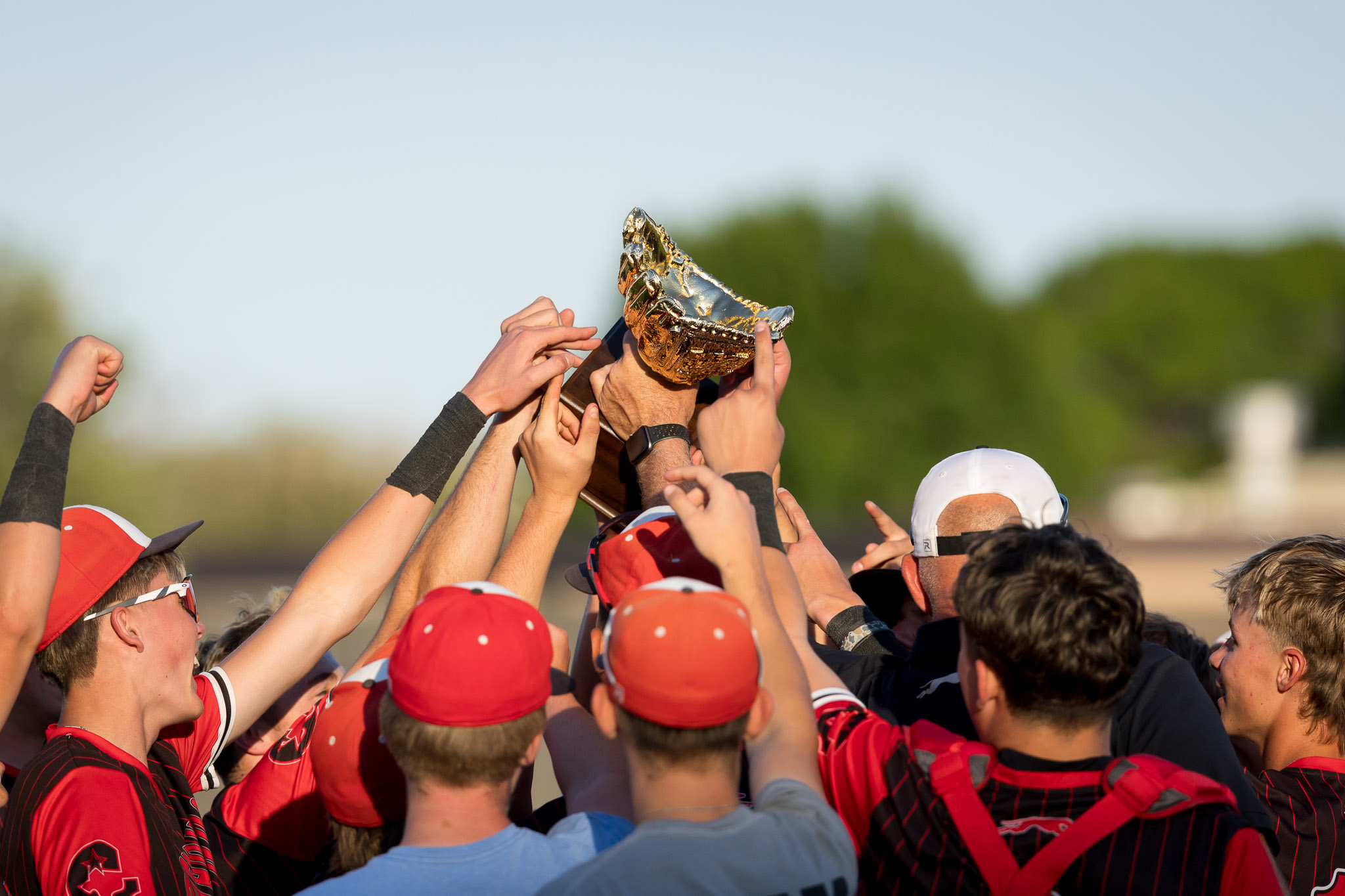 Team of athletes in red celebrate by lifting a shiny gold trophy together.