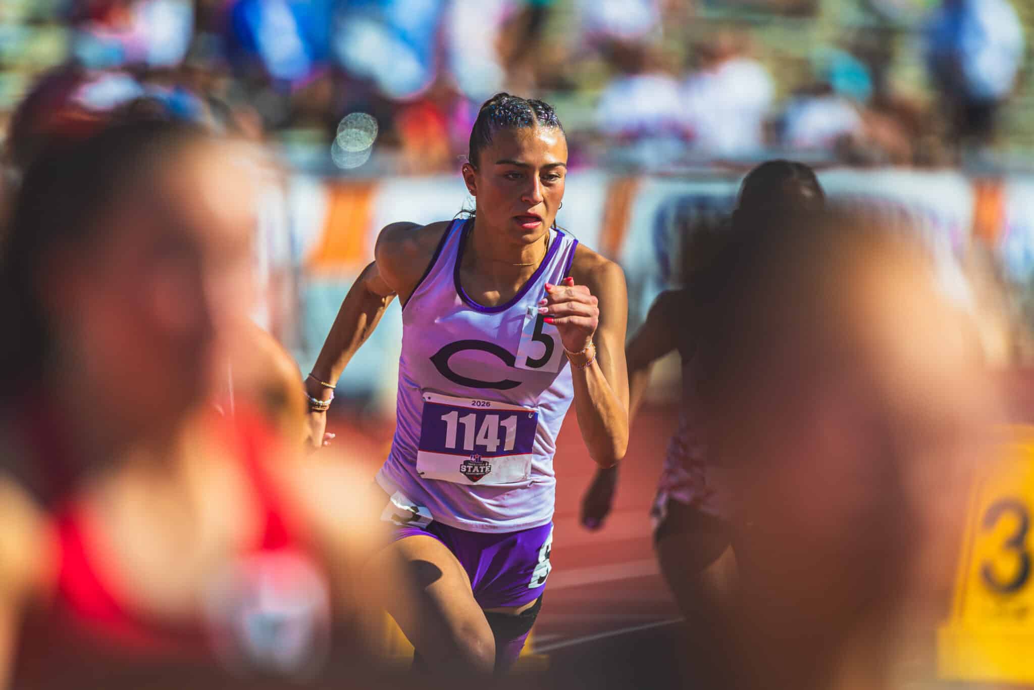 100A4520 | Press Pass Sports Female runner in purple athletic wear with bib 1141 powers forward during a crowded race.