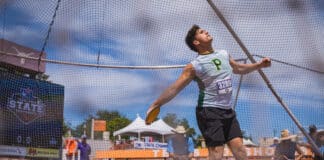 Male athlete in a white-green jersey with bib 3289, sprinting inside a fenced court during a race.
