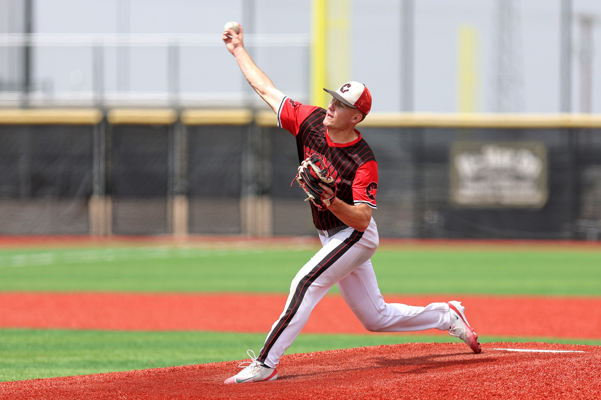 Baseball pitcher in red and black uniform throwing a ball on the mound with a blurred stadium background