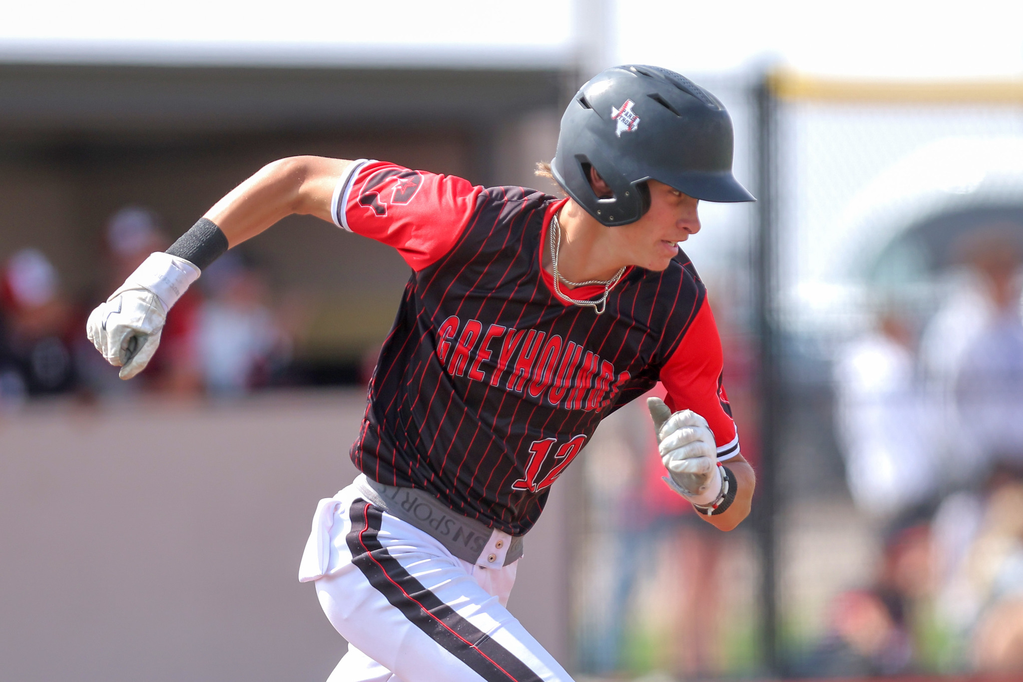 Baseball player in a dark helmet and red-and-black uniform sprinting on the field, jersey number 12 visible