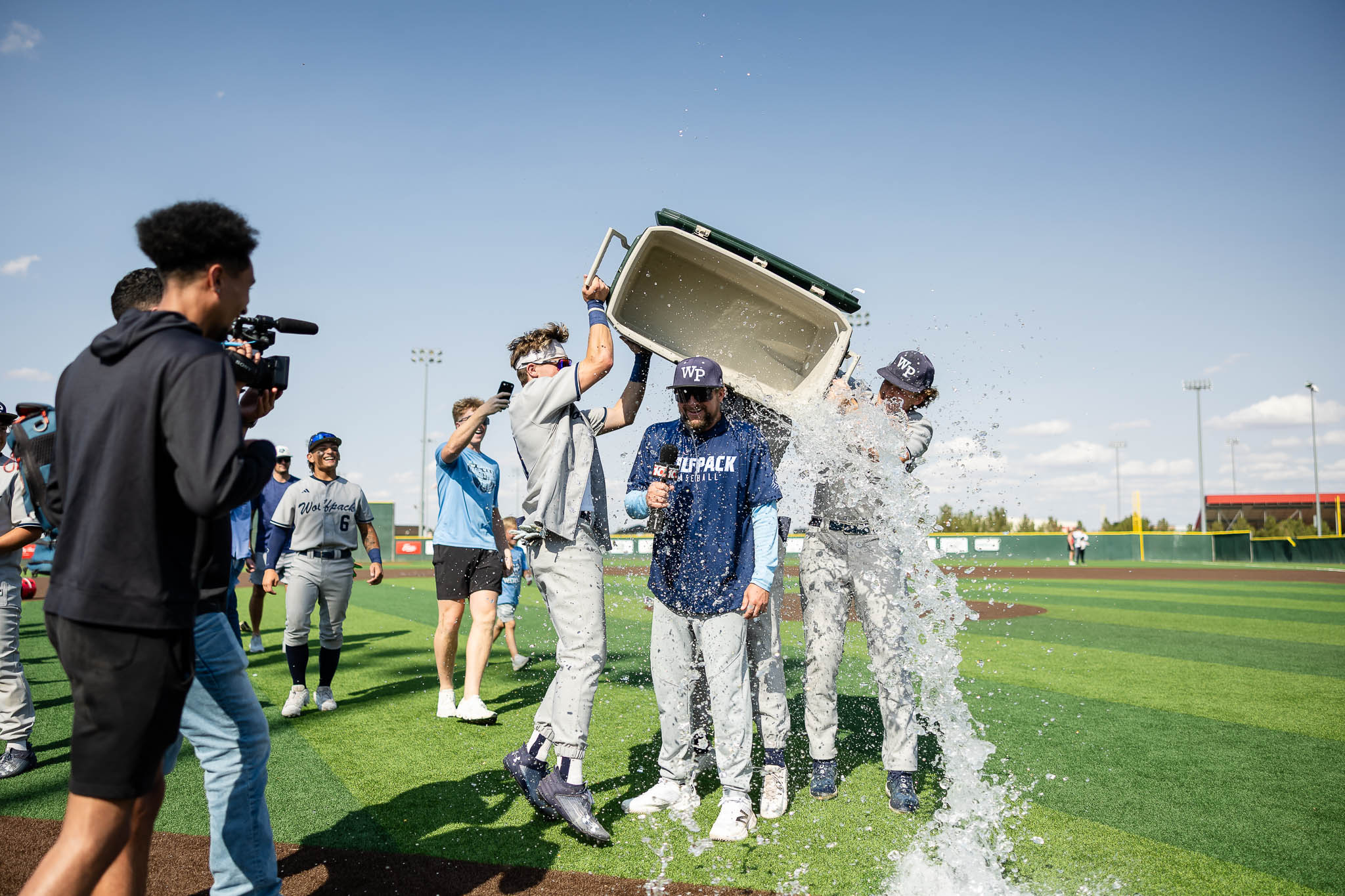 west-plains-baseball-jpegJoe-pps-13 | Press Pass Sports Baseball players celebrate on a field, lifting a cooler as water splashes around; a photographer records the moment.