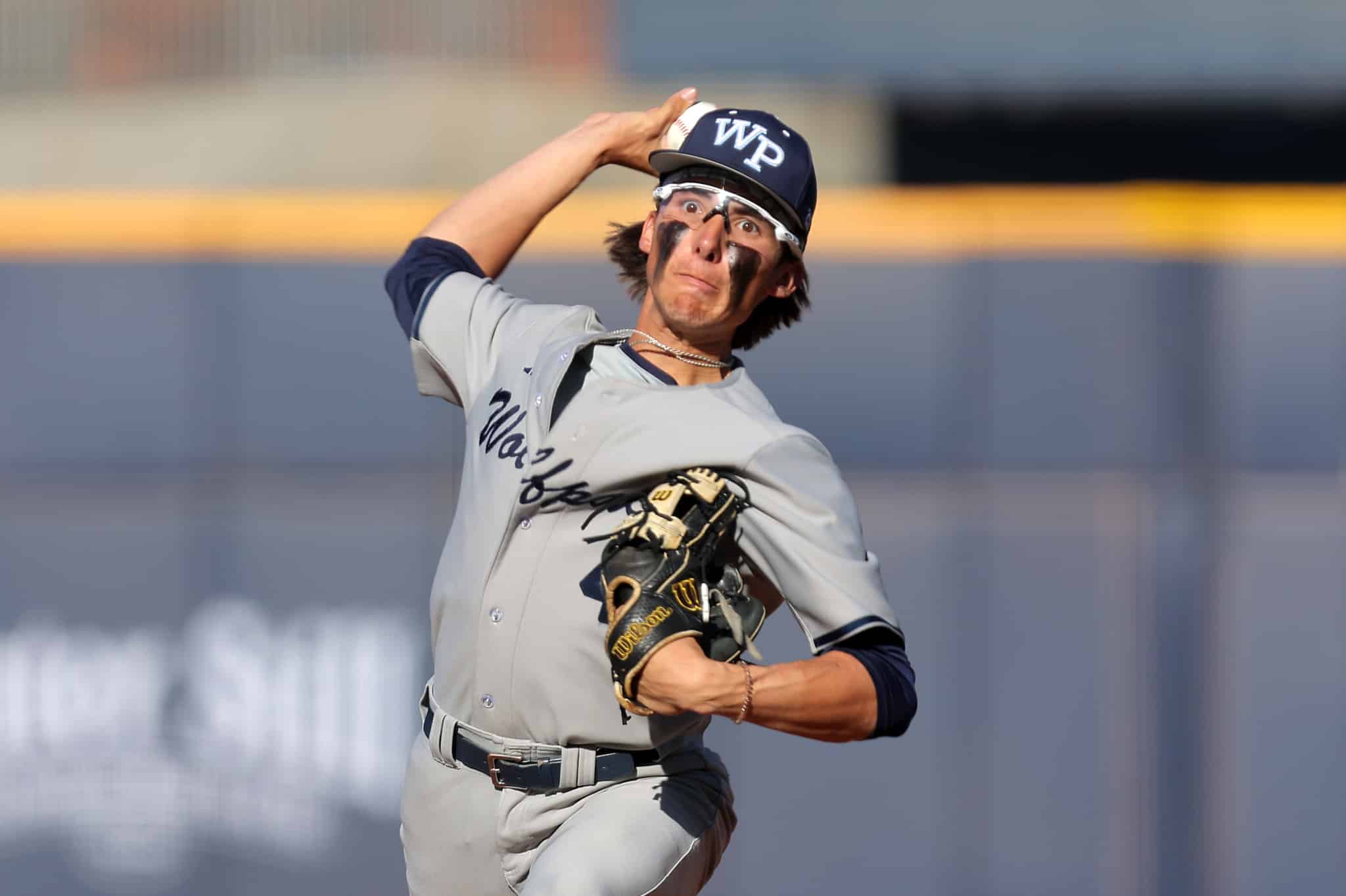 Baseball pitcher in a gray uniform delivers a pitch, wearing a dark cap with'WP' and a glove on his left hand.