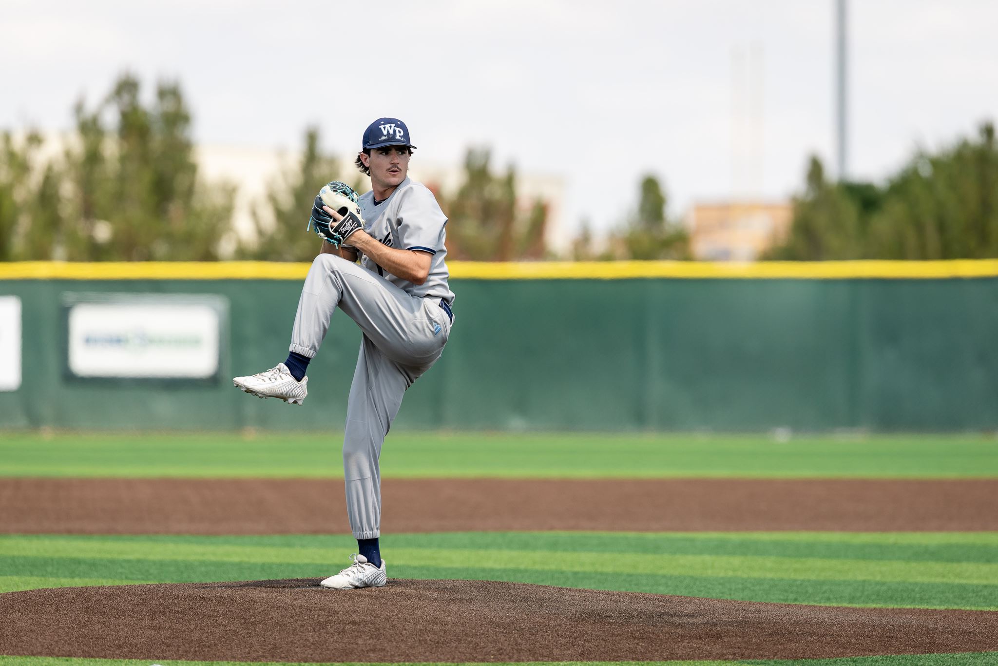 Baseball pitcher in gray uniform mid-windup on the mound, glove up and ready to throw.