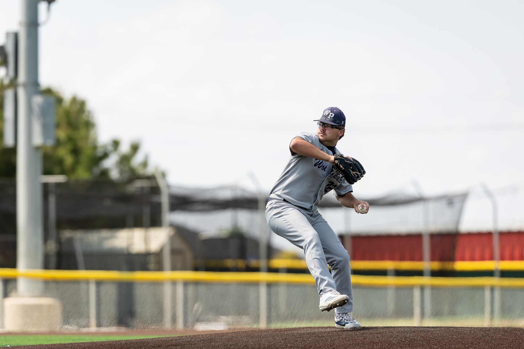 Baseball pitcher in a gray uniform delivering a pitch on the mound with a glove ready to throw.