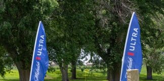 Blue vertical banners with white text stand beside trees on a grassy golf course; a yellow hole flag is visible in the distance.
