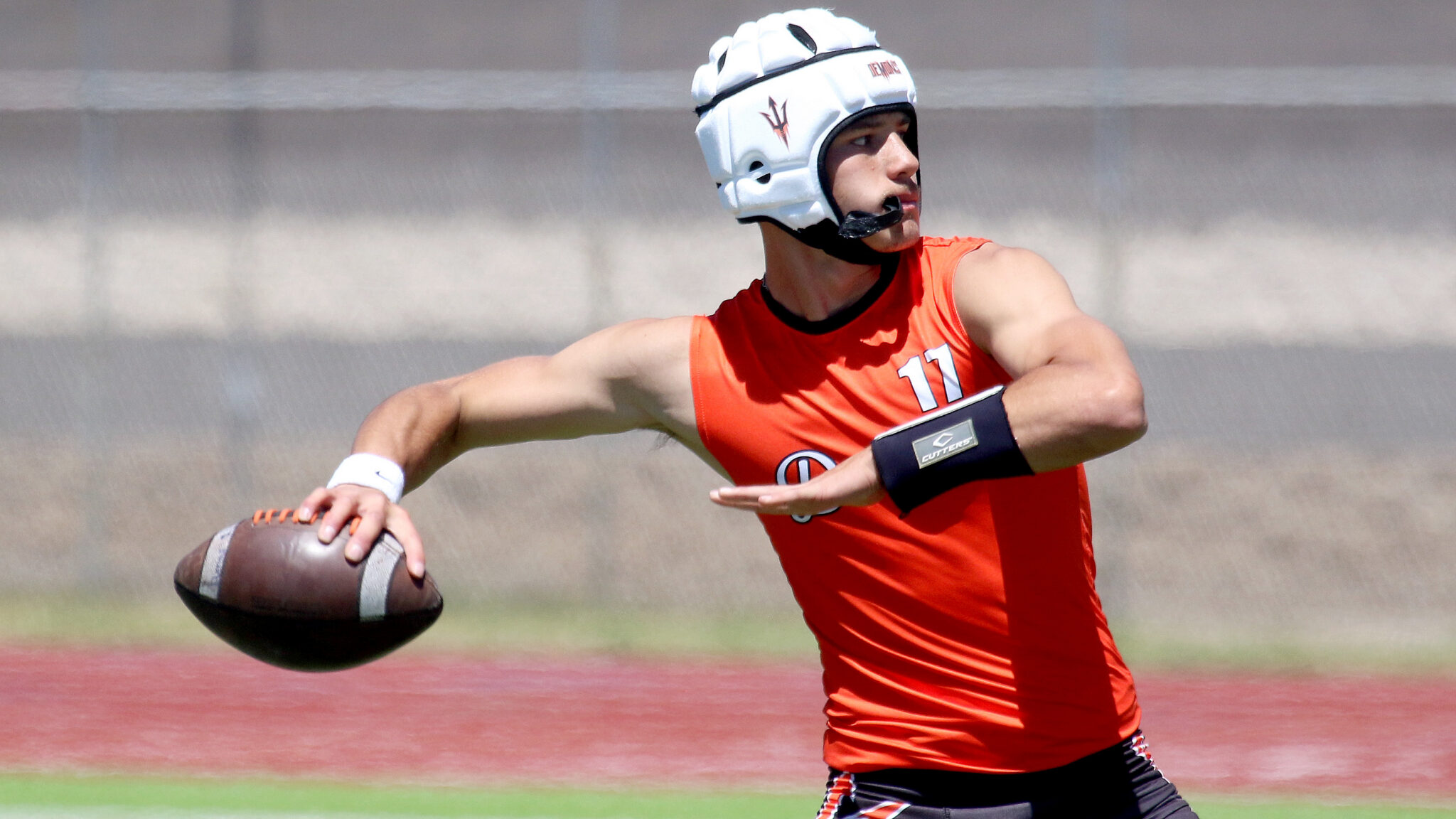 Colton Mills - Dumas - 7-on-7 - 053026 | Press Pass Sports Football player in an orange jersey and white helmet reaches to catch or pass the ball while running on a field.
