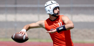 Football player in an orange jersey and white helmet reaches to catch or pass the ball while running on a field.