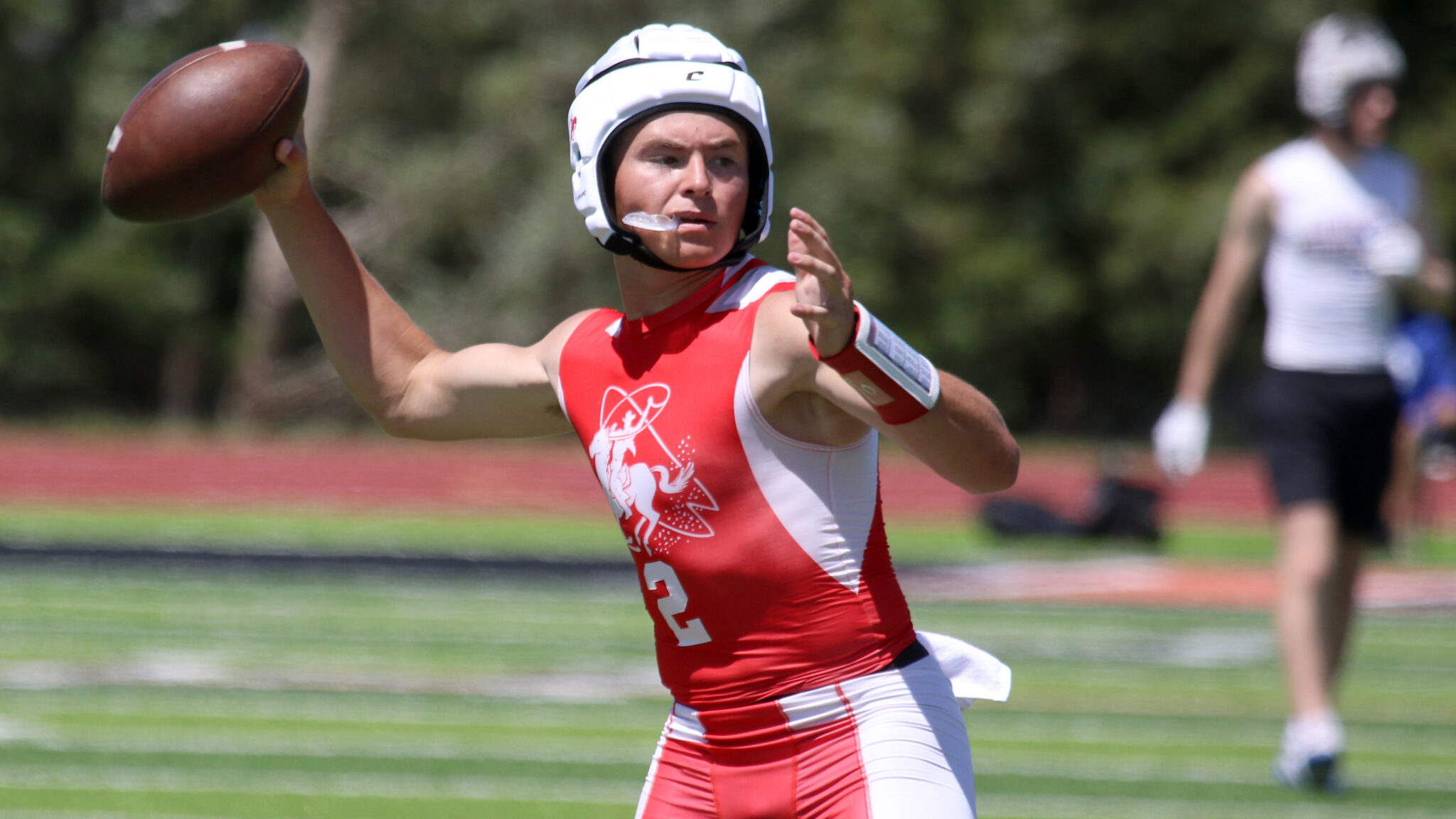 Cooper Schilling - Perryton - 7-on-7 - 053026 | Press Pass Sports Female football player in a red and white uniform throws a football on a field, wearing a white helmet.