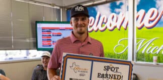 Smiling man in a red striped polo holds a large 'Spot Earned! 2020' certificate with logos at an indoor award event.