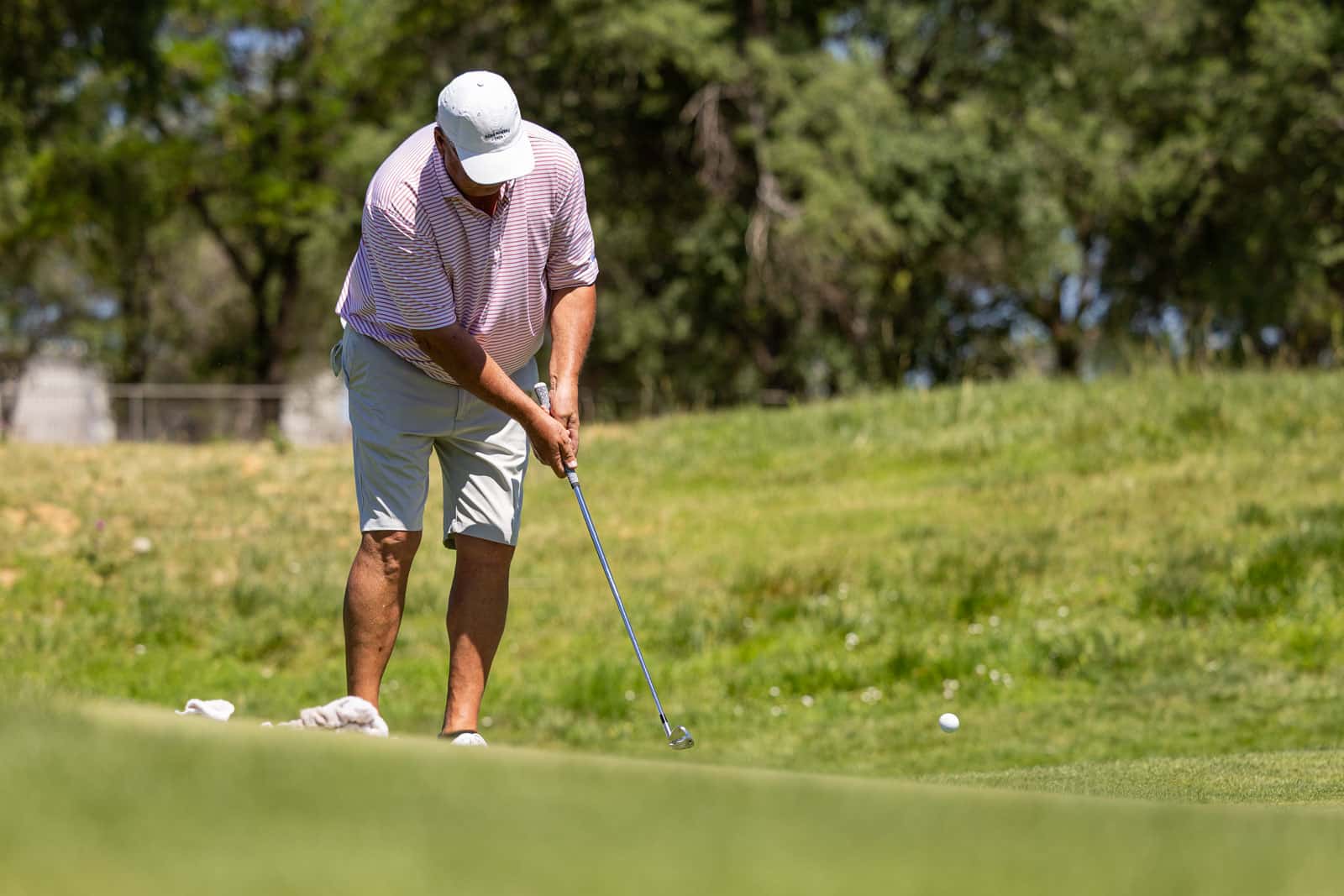 Golfer bending over to putt on a sunny green golf course, preparing to strike the ball with a putter.
