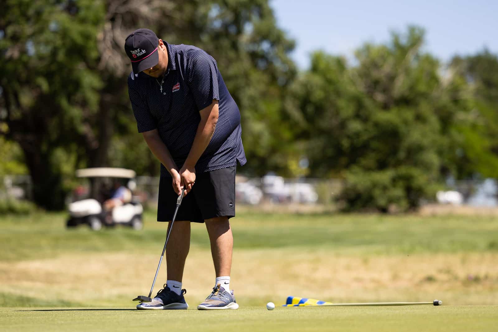 Golfer lining up a putt on a sunny golf course, bent over the ball with a putter in hand.