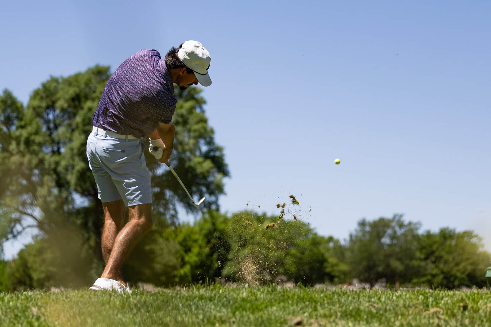 Golfer mid-swing on a sunny course, dirt spraying as he hits a golf ball.