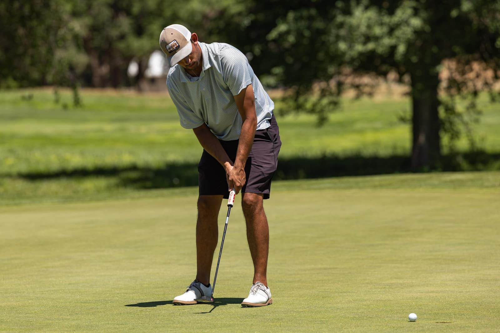 Golfer lining up a putt on a sunny golf green with a white ball nearby.
