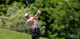 Golfer in a striped polo swinging a club on a grassy fairway, sending dirt and grass into the air as he follows through.