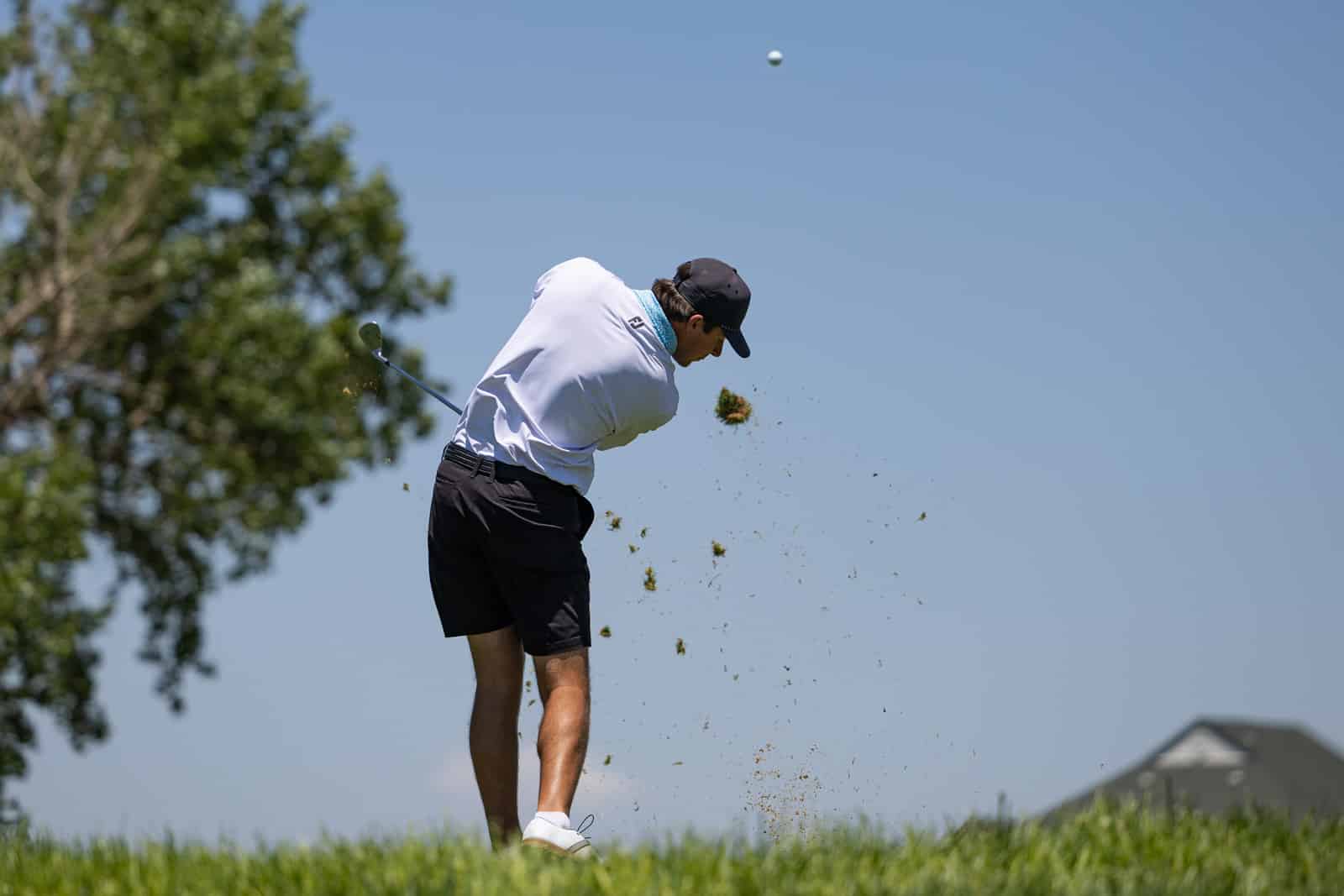 Golfer mid-swing on a sunny day, grass and dirt spraying as he hits the ball
