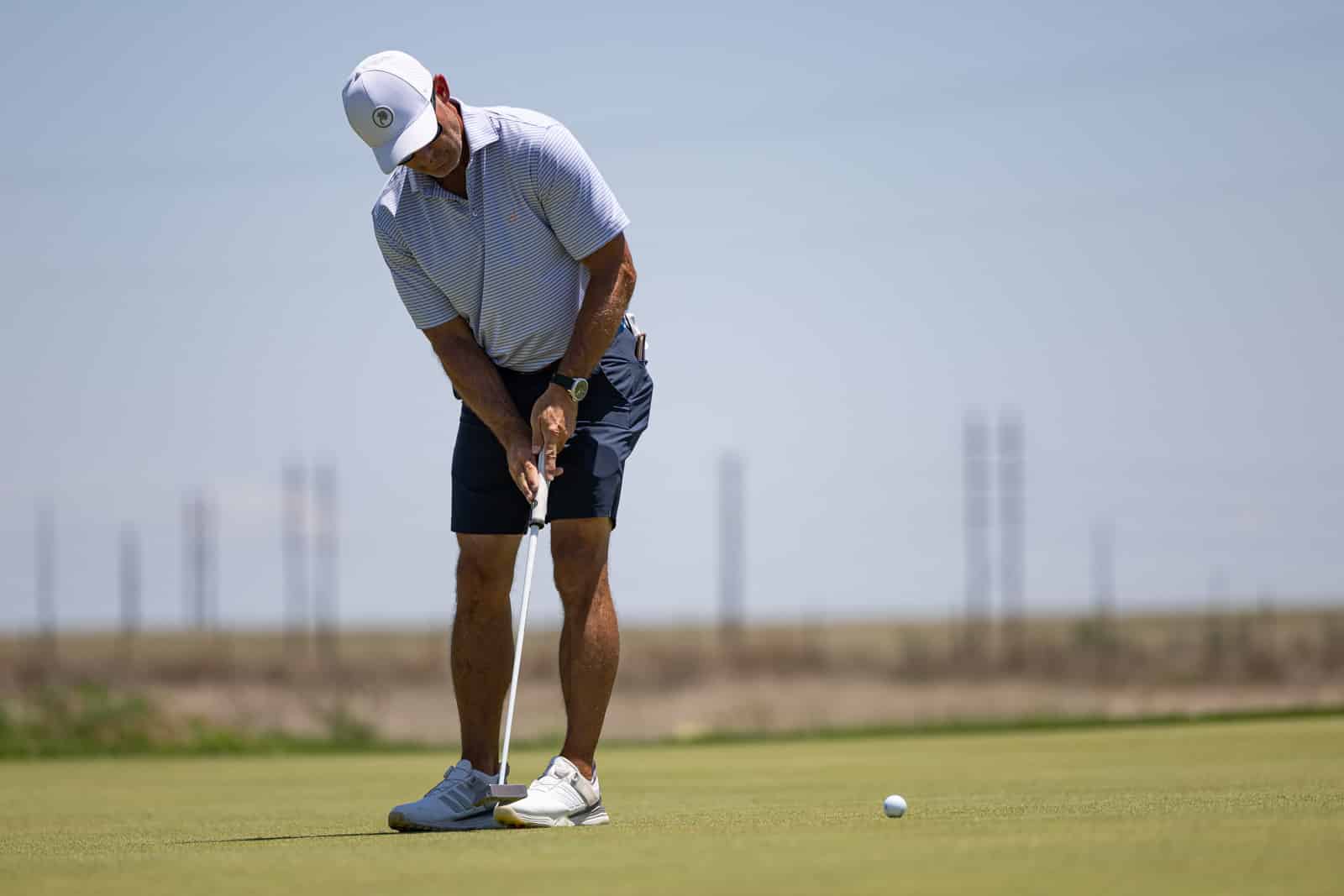 Golfer lining up a putt on a green, preparing to stroke the ball toward the hole.