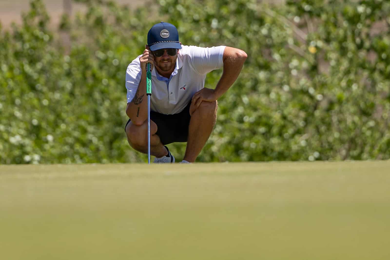 Golfer crouching on the putting green, reading the break with a putter in hand.