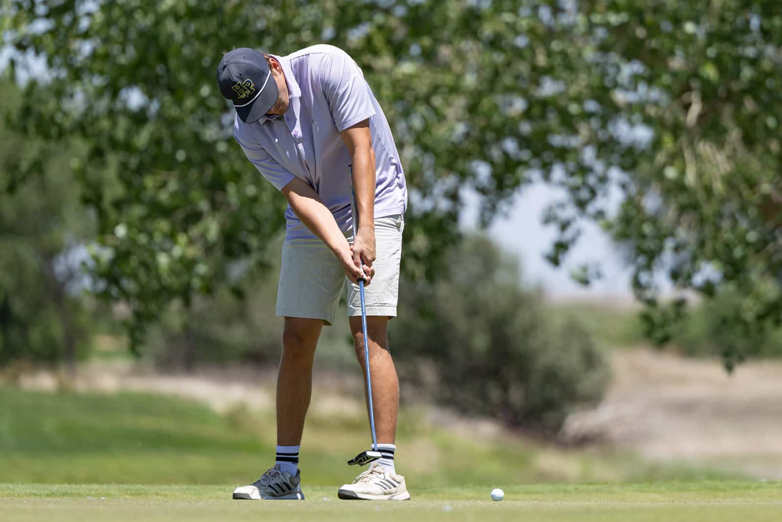 Golfer bending over to putt on a green, preparing to strike the ball on a sunny day
