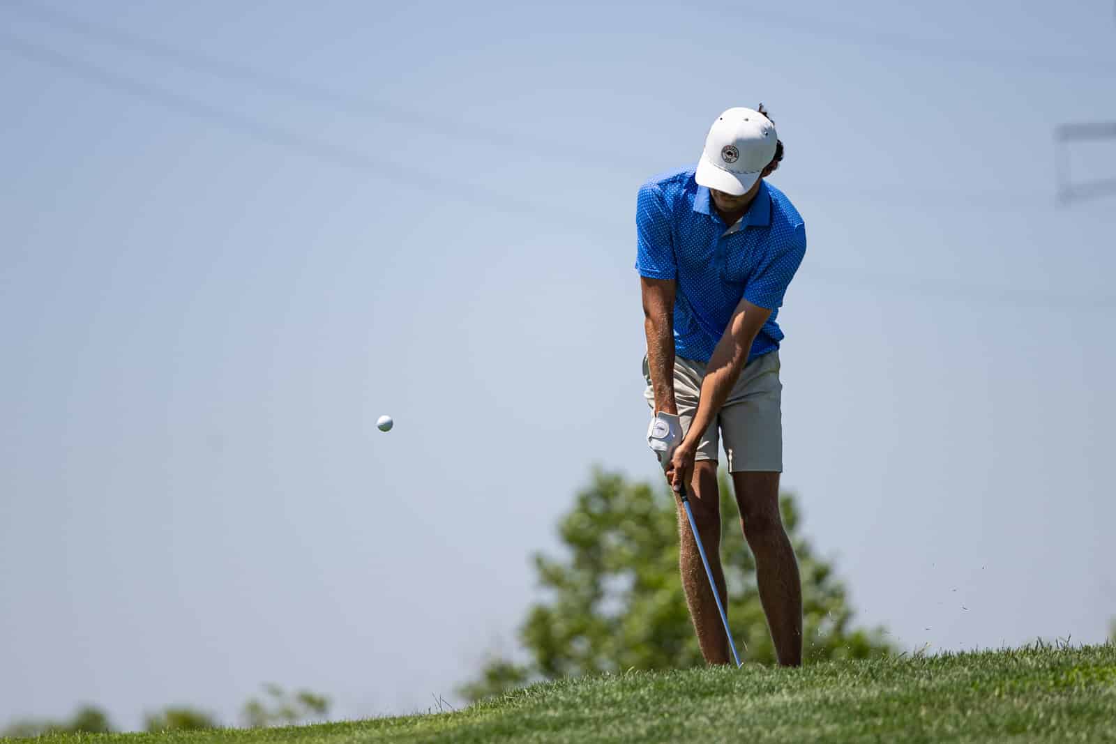 Golfer in a blue polo and white cap preparing to swing on a sunny golf course.