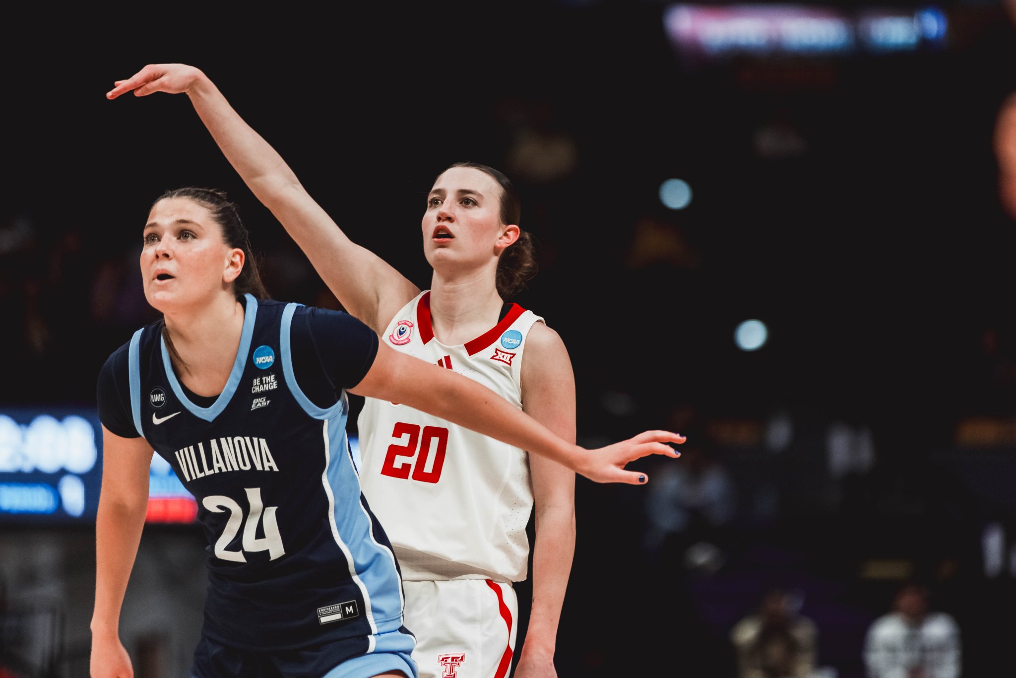 Two female college basketball players reach upward during a game: one in navy Villanova kit (#24) and the other in white (#20).