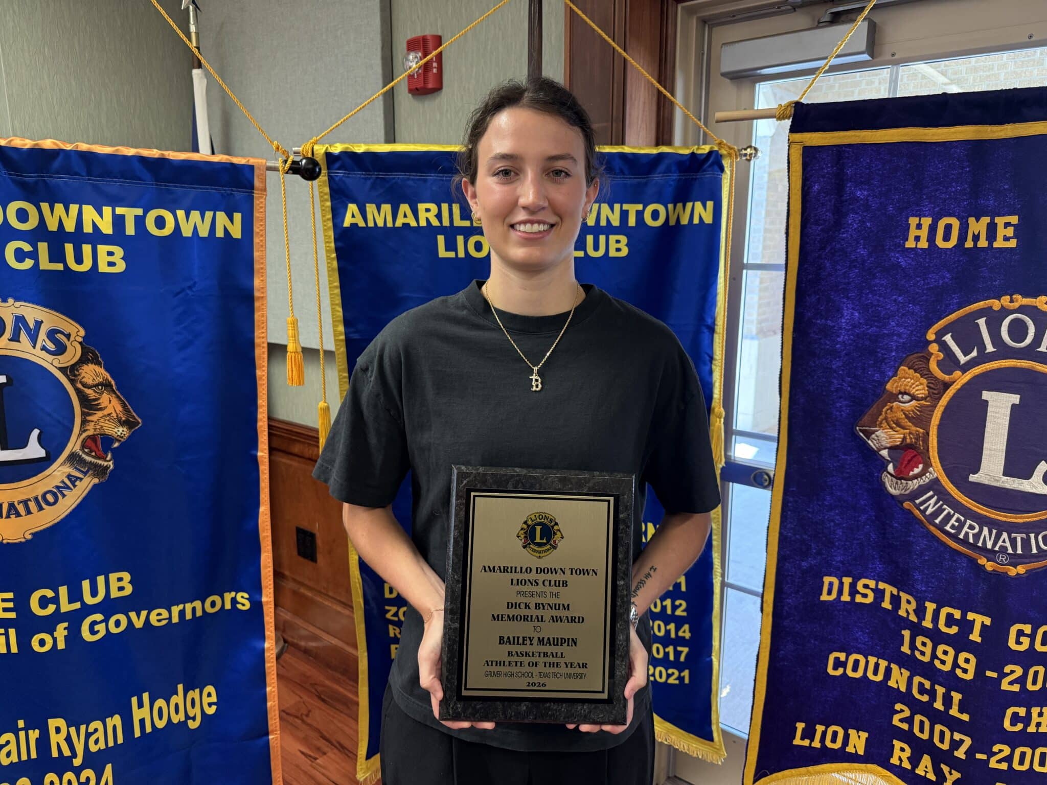 Young woman standing in front of Amarillo Downtown Lions Club banners, holding a framed award plaque.