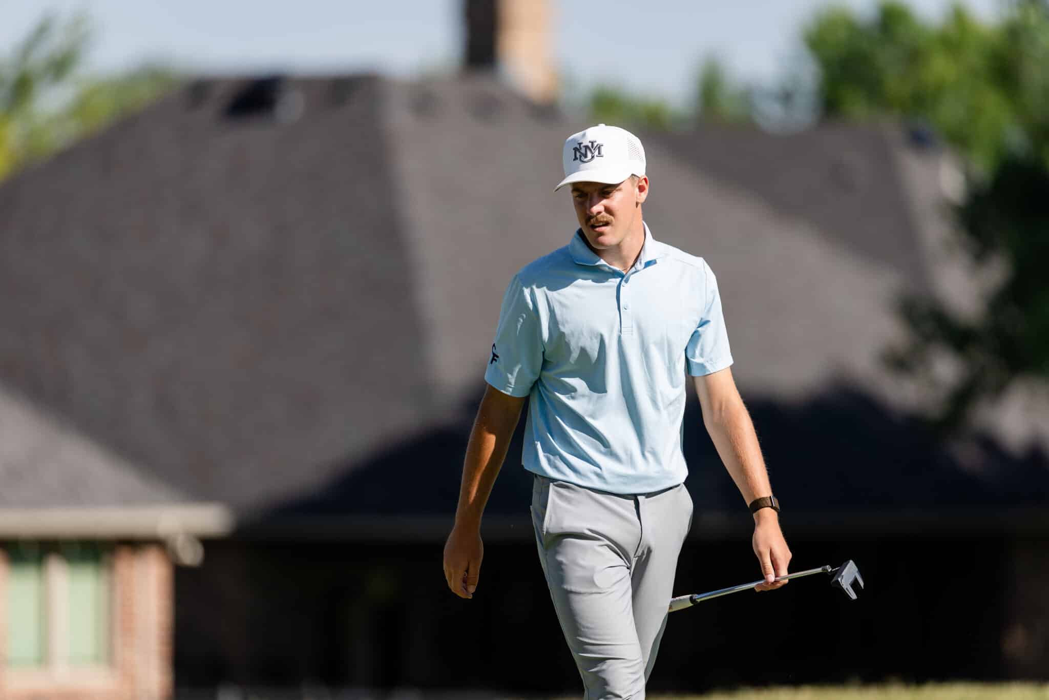 Korn Ferry Occunet Classic Day 1 | Press Pass Sports Golfer in a light blue polo and white cap walking on the course, holding a golf club.