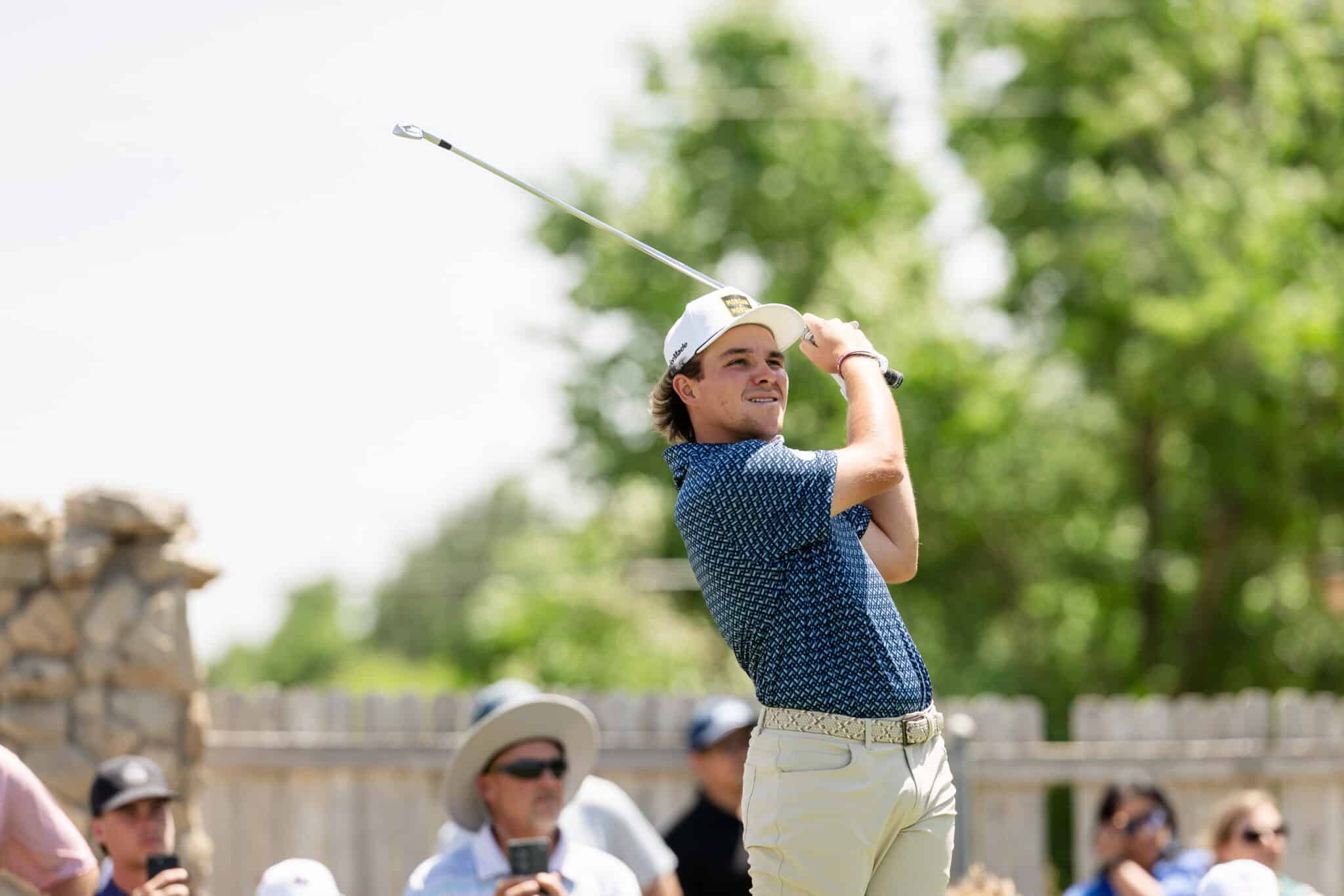 korn-ferry-occunet-classic-day-1-jpegJoe-303 | Press Pass Sports Golfer in a white cap and blue patterned shirt mid-swing on a sunny day, with spectators in the background.