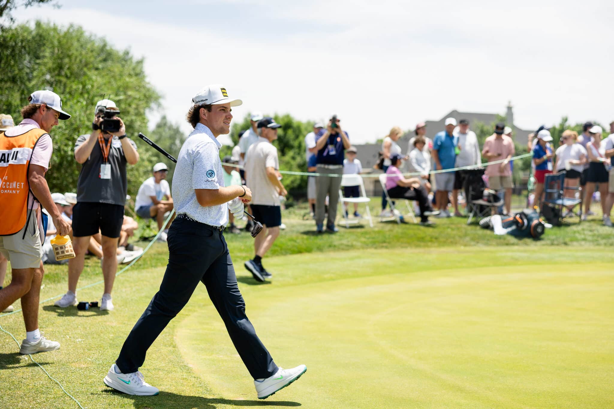 korn-ferry-occunet-classic-day-2-jpegJoe-376 | Press Pass Sports Male golfer in a light blue shirt and white cap walks across the fairway while spectators and photographers watch from the sidelines.