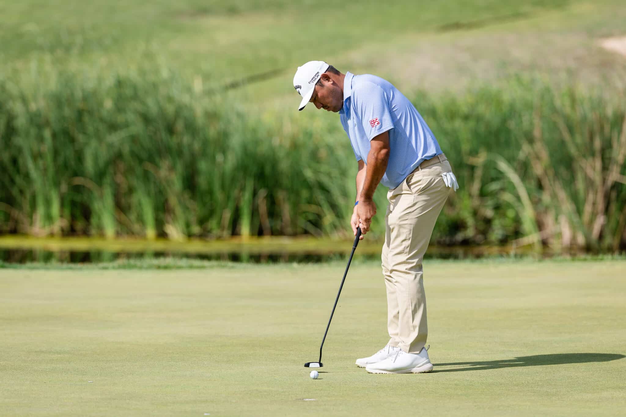 korn-ferry-occunet-classic-day-2-jpegJoe-523 | Press Pass Sports Golfer lining up a putt on a green, wearing a light blue polo, beige pants, and a white cap with a putter in hand.