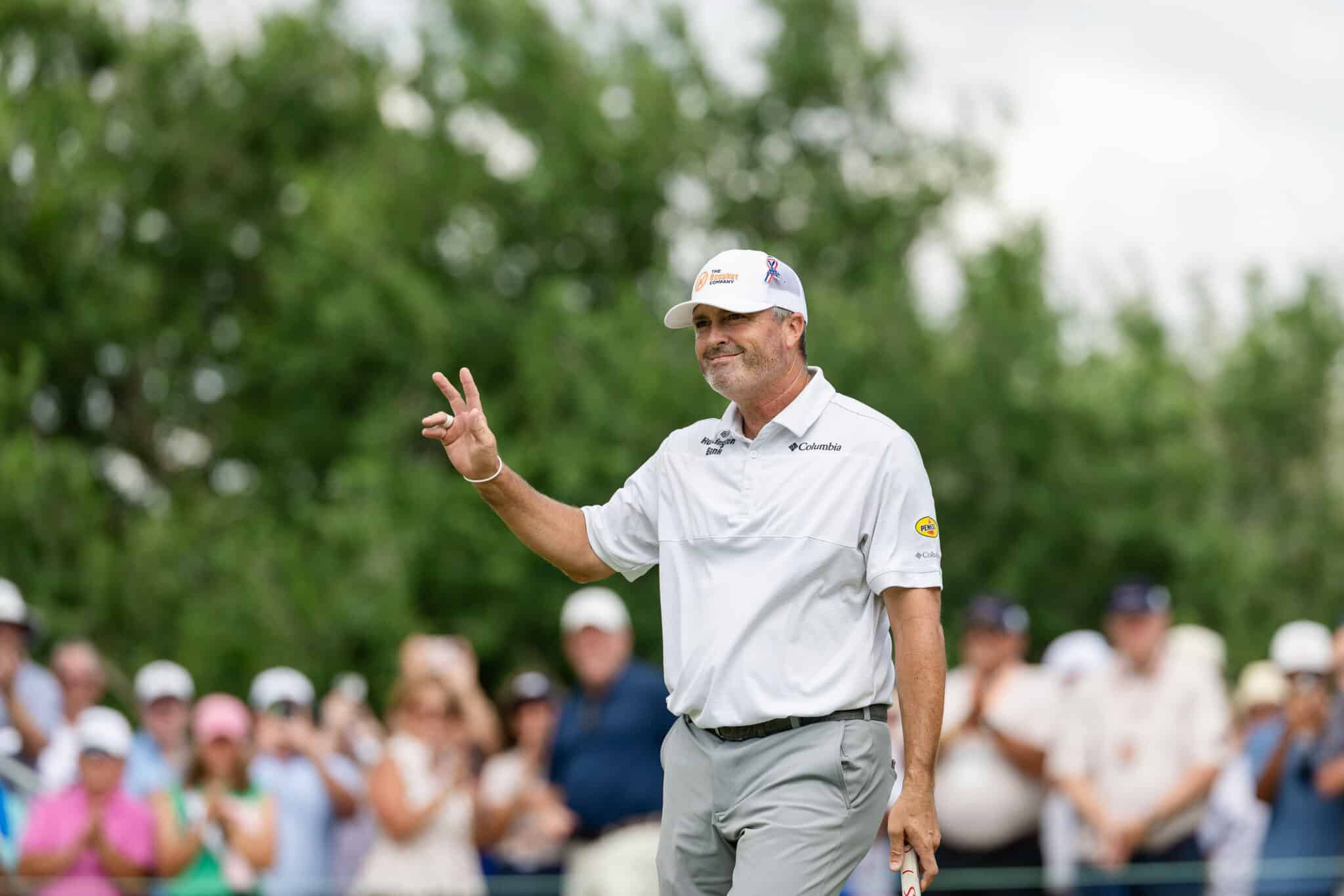 korn-ferry-occunet-classic-day-2-jpegJoe-493 | Press Pass Sports Male golfer in a white polo and cap waves to cheering spectators during a tournament.