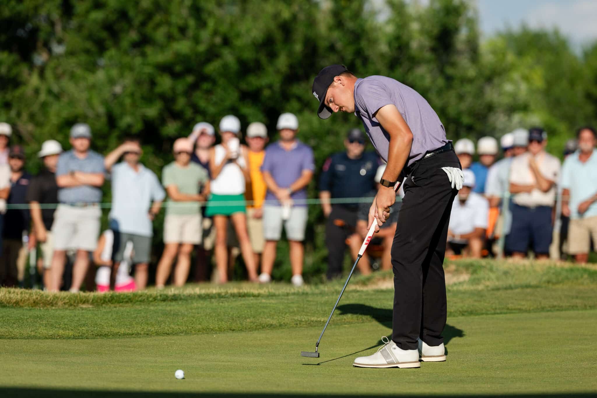 korn-ferry-occunet-classic-day-2-jpegJoe-573 | Press Pass Sports Golfer in a gray shirt and black cap lining up a putt on the green as spectators watch in the background.
