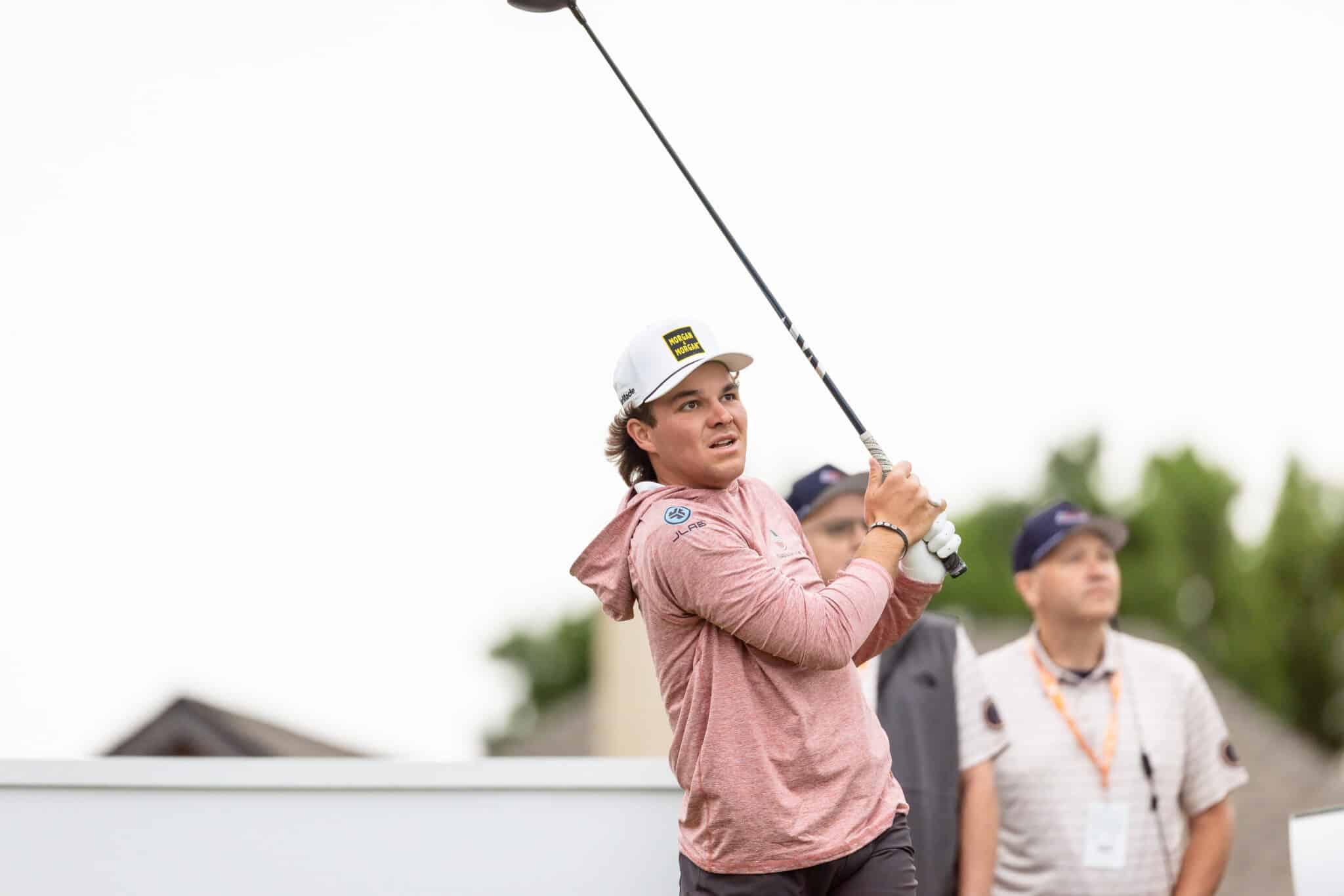 korn-ferry-tour-occunet-classic-day-5-jpegJoe-12 | Press Pass Sports Golfer in pink shirt and white cap mid-swing on a golf course, focused on ball follow-through with others watching in the background.