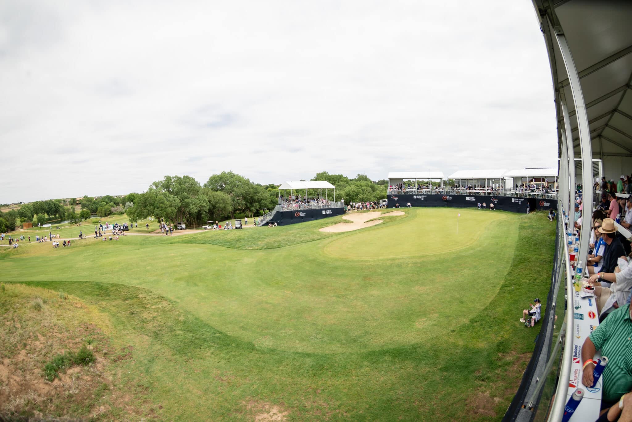 korn-ferry-tour-occunet-classic-day-5-jpegJoe-326 | Press Pass Sports Wide-angle view of a golf tournament with spectators in tiered stands along the right side and a grassy fairway below.