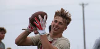 Young male football player in beige jersey catching a brown football with white and red gloves during a game outdoors.