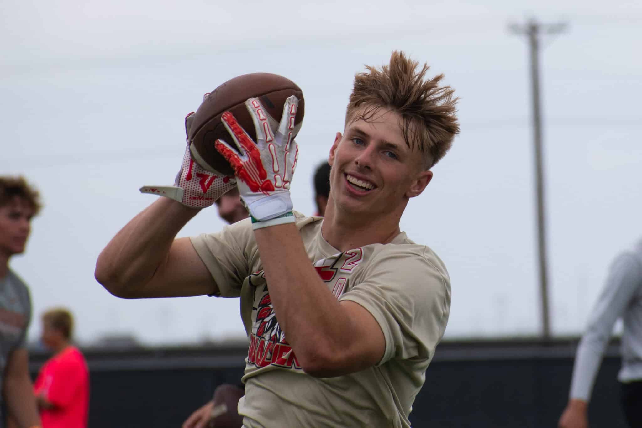 DSC_0079 | Press Pass Sports Young male football player in beige jersey catching a brown football with white and red gloves during a game outdoors.