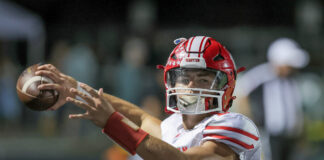 Quarterback in red-and-white uniform throws a football during a game, arm extended for a pass.