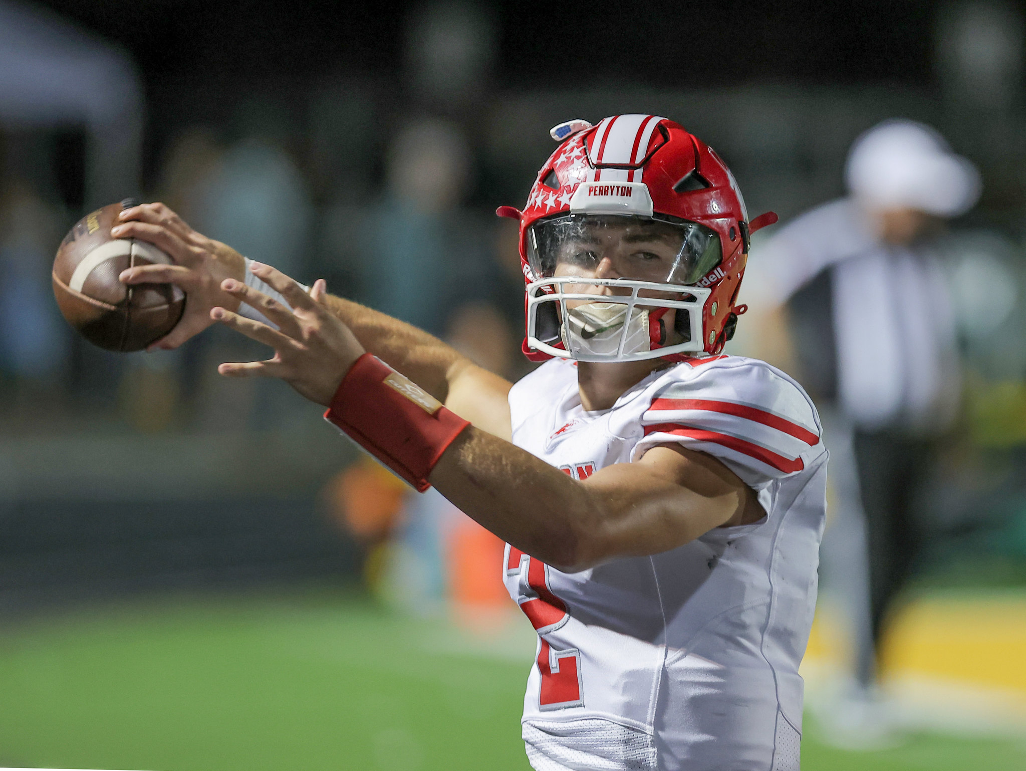 Quarterback in red-and-white uniform throws a football during a game, arm extended for a pass.