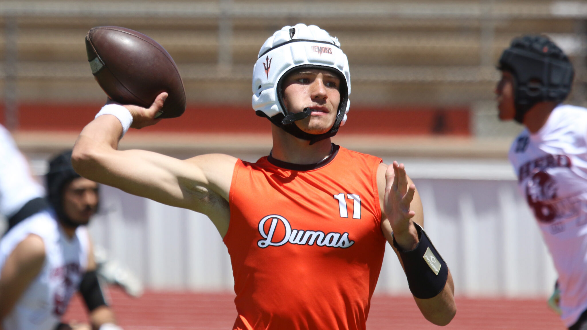 Colton Mills - Dumas - 7-on-7 - 053026 - 1 | Press Pass Sports Athlete in orange jersey (number 11) throws a football during a game, wearing a white helmet and shield, with teammates in the background.