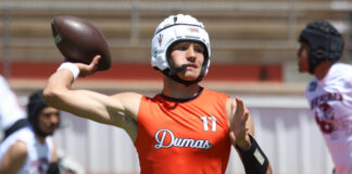 Athlete in orange jersey (number 11) throws a football during a game, wearing a white helmet and shield, with teammates in the background.