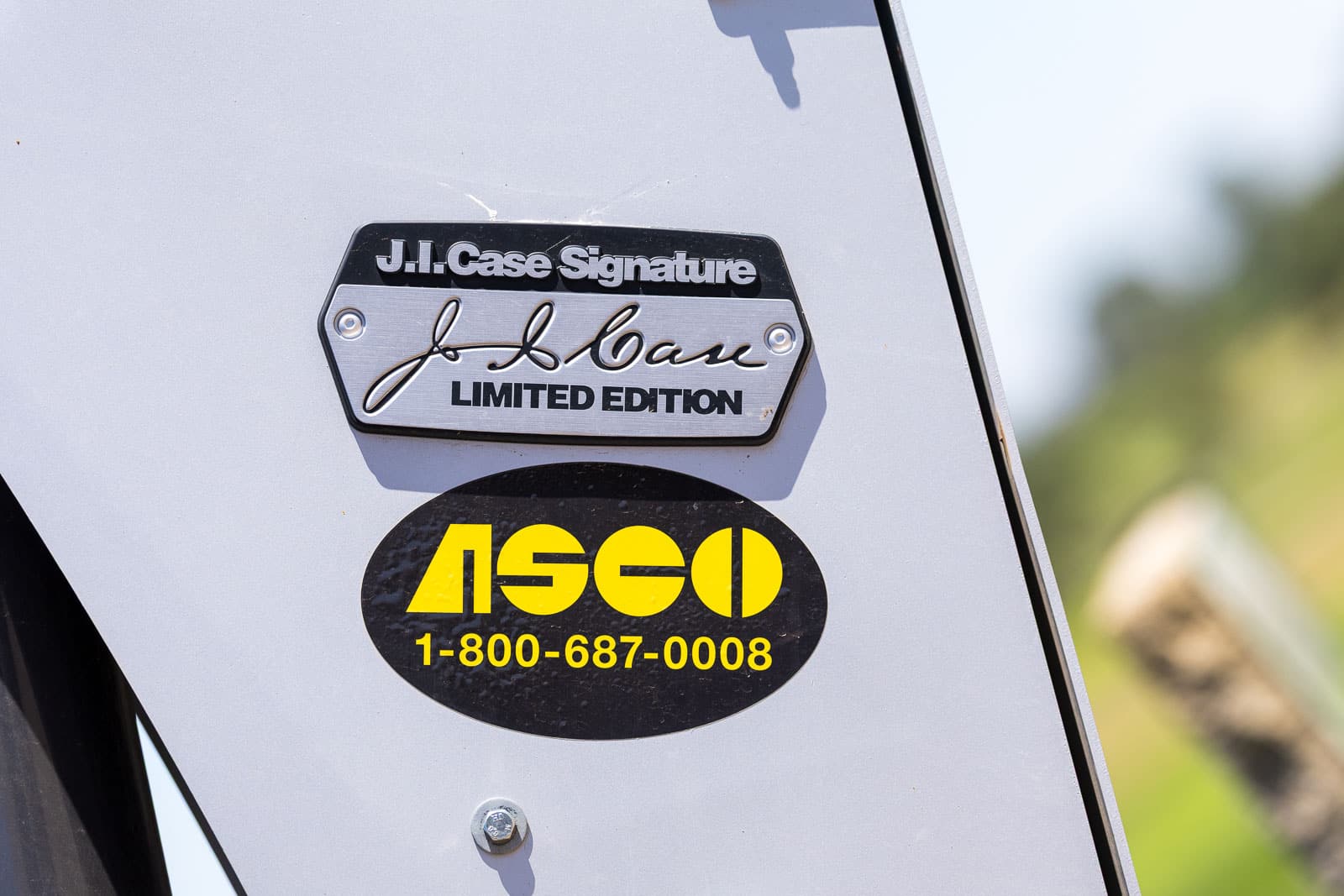 Close-up of a vehicle tail showing a J.I. Case Signature Limited Edition badge and a black oval sticker with yellow letters and the phone number 1-800-687-0008.