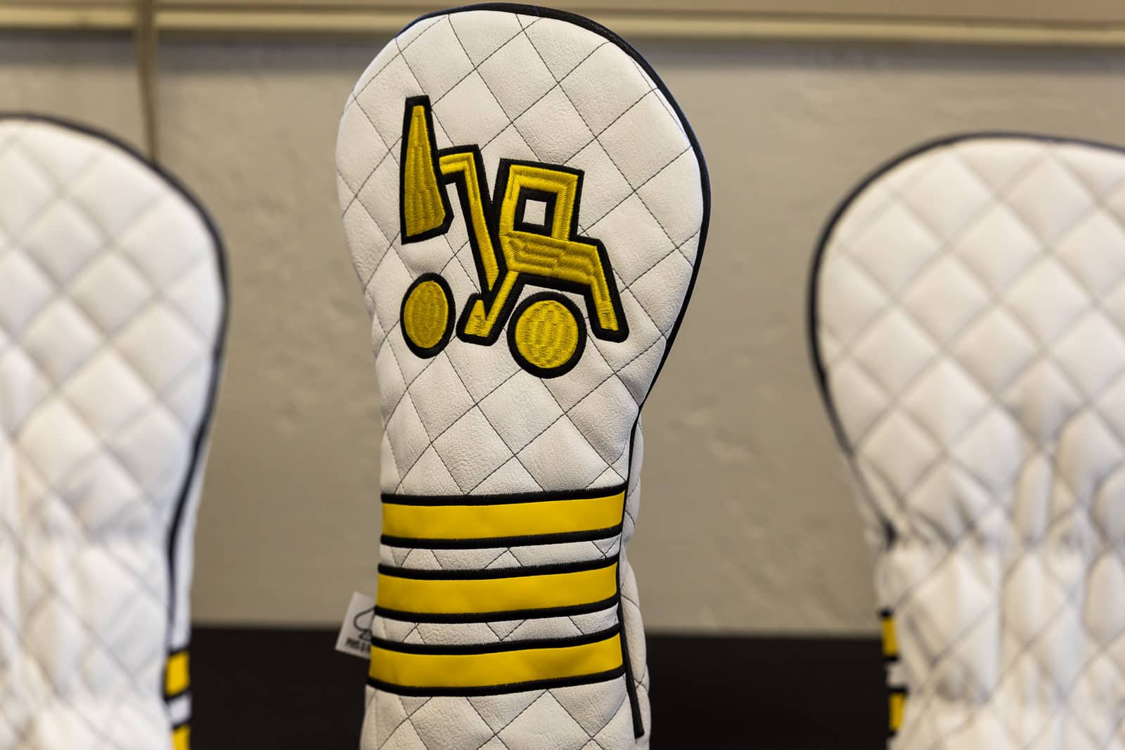 White quilted glove with a yellow forklift icon embroidered on the back, black and yellow cuff stripes visible